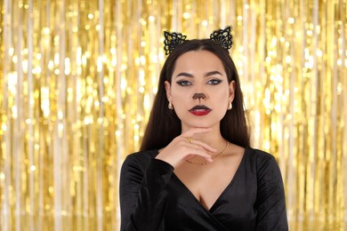 Photo of Beautiful woman with cat makeup and ears on golden background