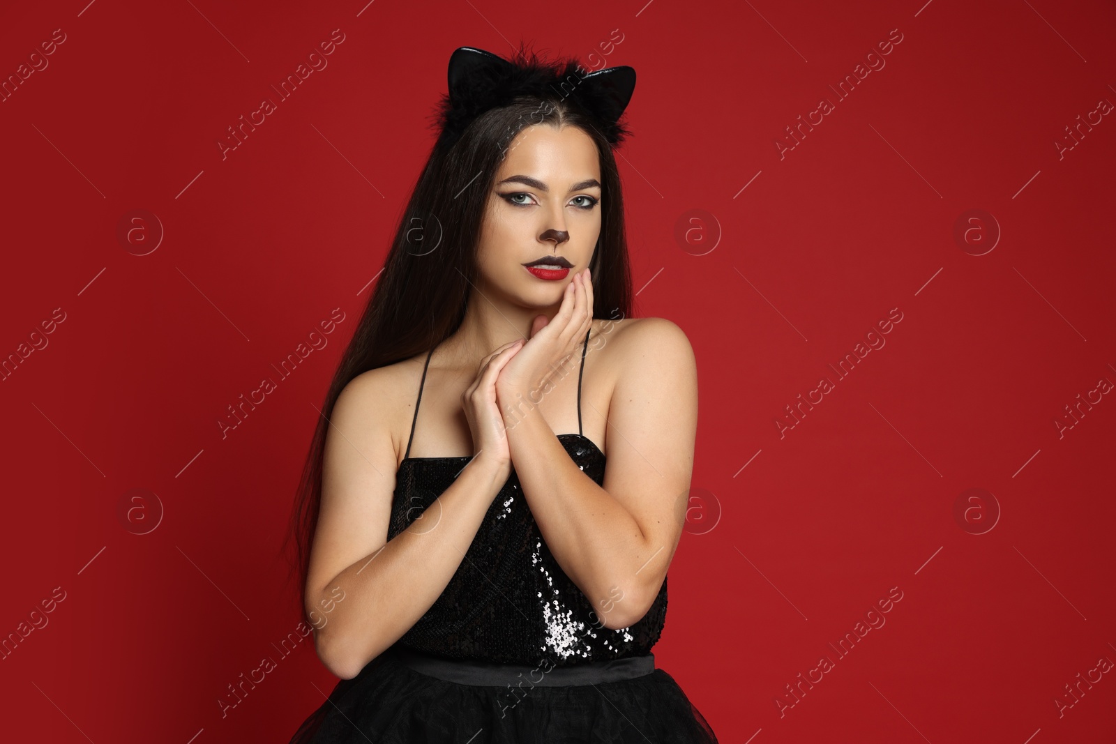 Photo of Woman with cat makeup and ears in beautiful dress on red background