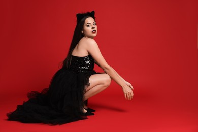 Photo of Woman with cat makeup and ears in beautiful dress on red background. Space for text