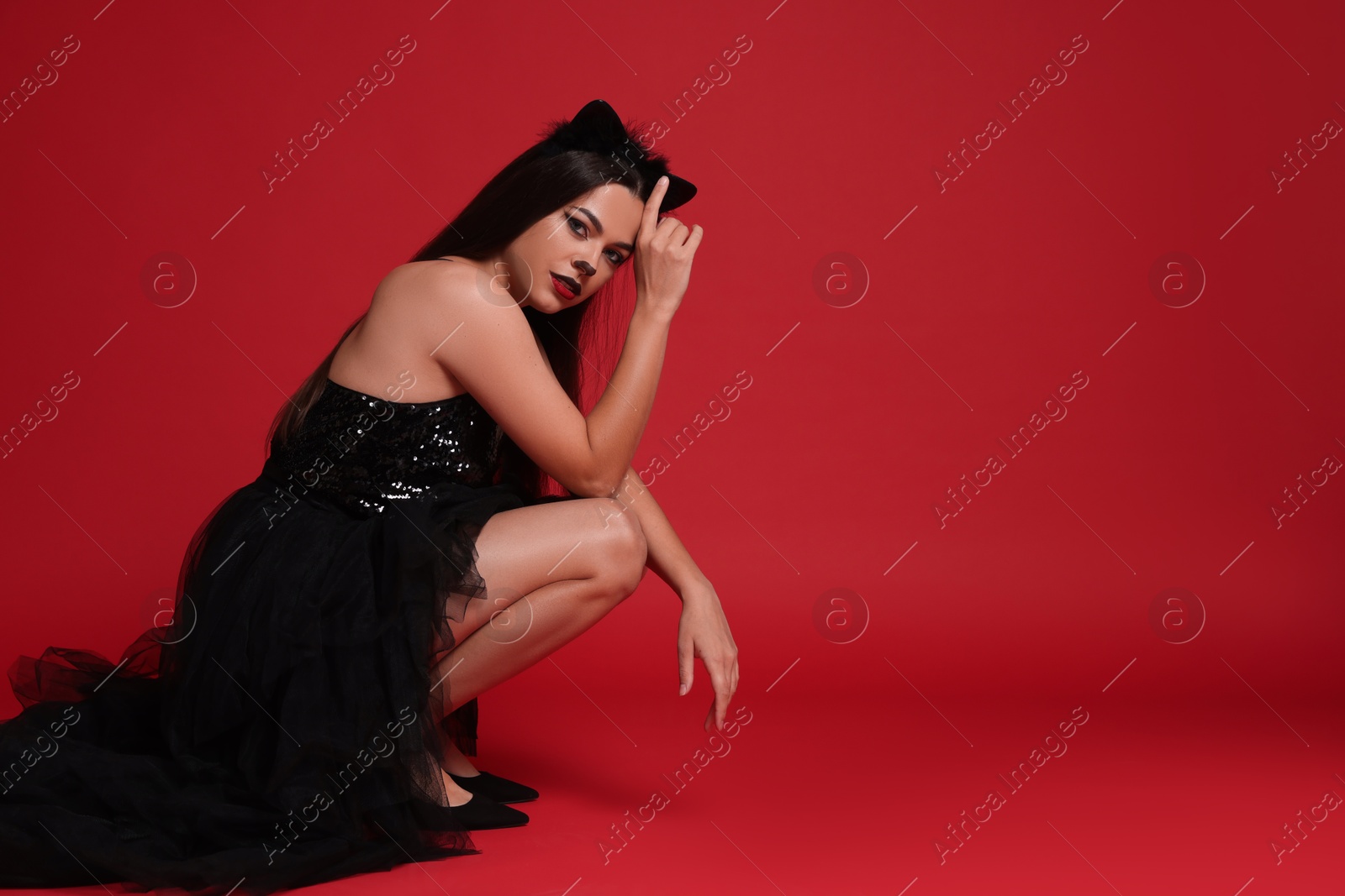 Photo of Woman with cat makeup and ears in beautiful dress on red background. Space for text