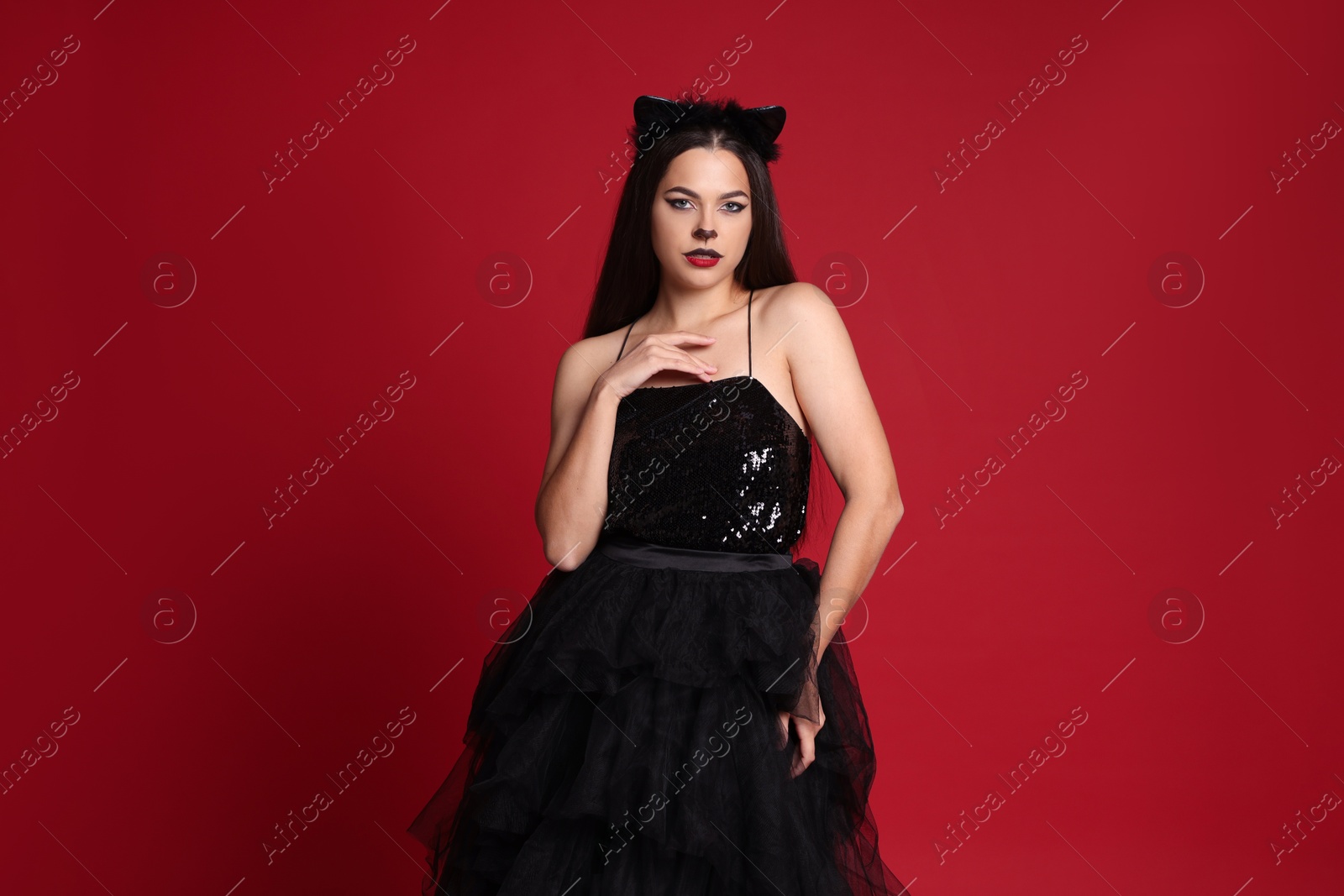 Photo of Woman with cat makeup and ears in beautiful dress on red background