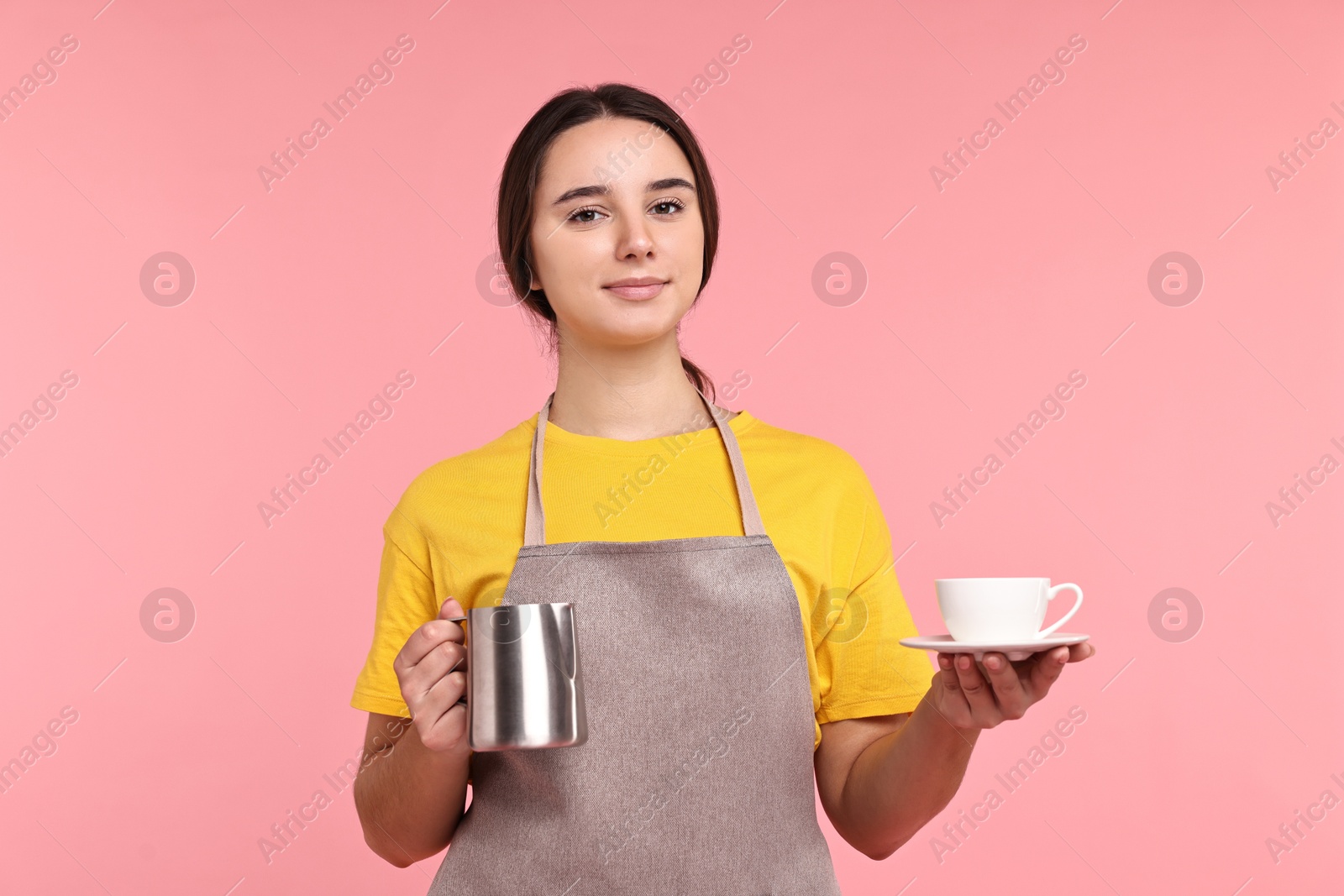 Photo of Girl in apron with pitcher and cup of coffee on pink background. Work for teenagers