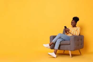 Photo of Smiling woman with smartphone sitting in armchair on yellow background. Space for text