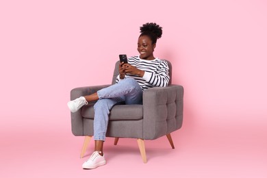 Photo of Smiling woman with smartphone sitting in armchair on pink background