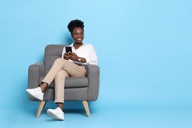 Photo of Smiling woman with smartphone sitting in armchair on light blue background. Space for text