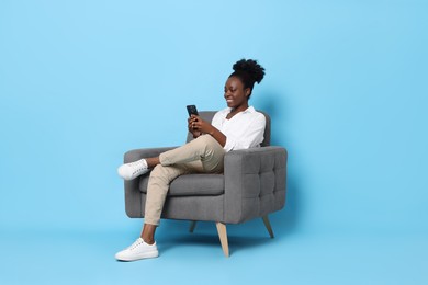 Photo of Smiling woman with smartphone sitting in armchair on light blue background