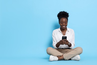 Photo of Happy woman with smartphone on light blue background. Space for text