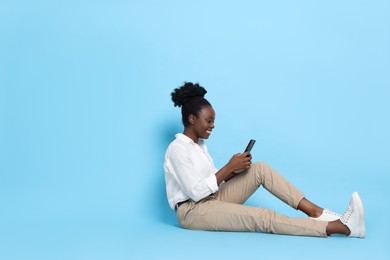 Photo of Happy woman with smartphone on light blue background. Space for text