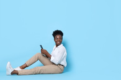 Photo of Happy woman with smartphone on light blue background. Space for text