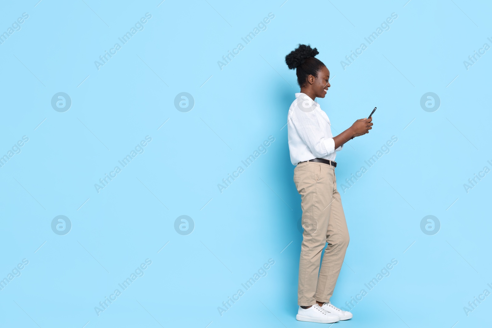 Photo of Happy woman with smartphone on light blue background. Space for text