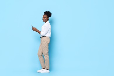 Photo of Happy woman with smartphone on light blue background. Space for text