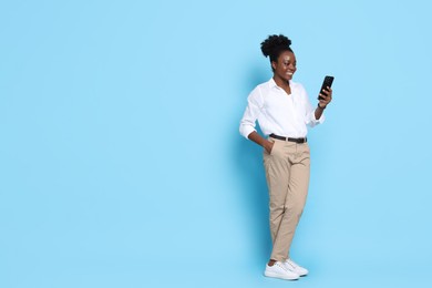 Photo of Happy woman with smartphone on light blue background. Space for text