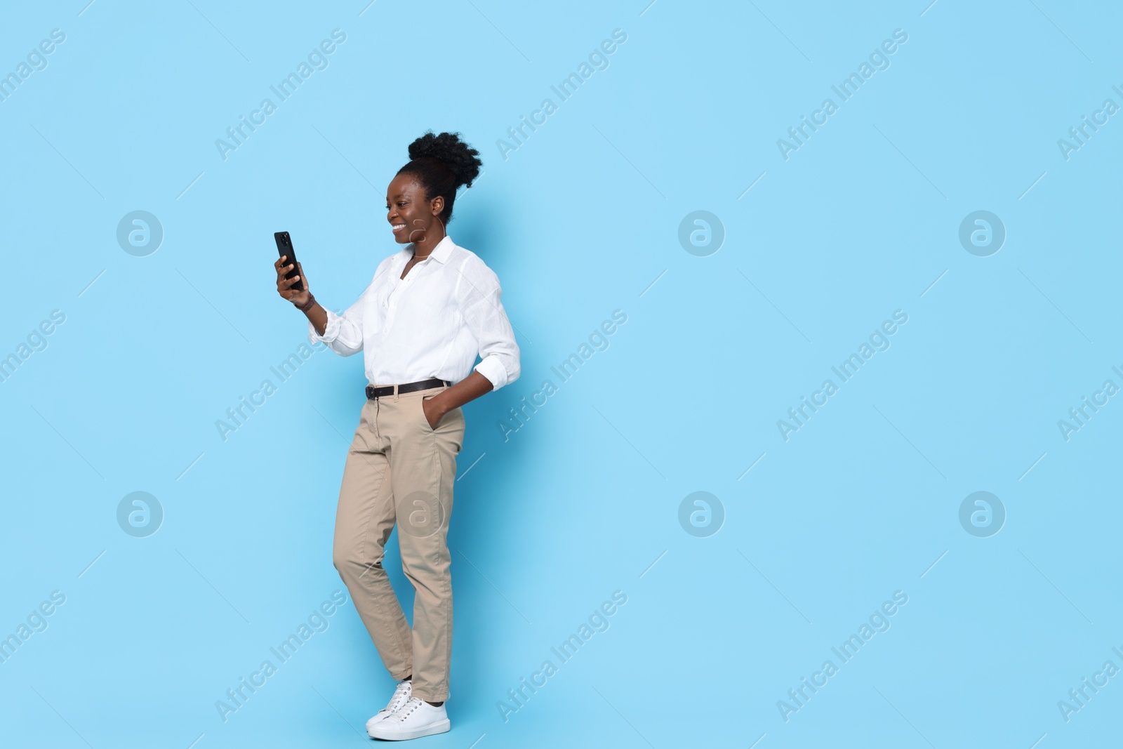 Photo of Happy woman with smartphone on light blue background. Space for text