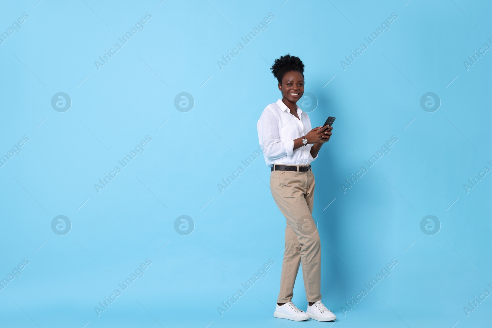 Photo of Happy woman with smartphone on light blue background. Space for text