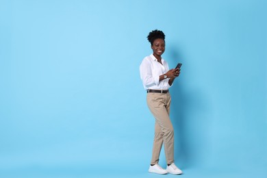 Photo of Happy woman with smartphone on light blue background. Space for text