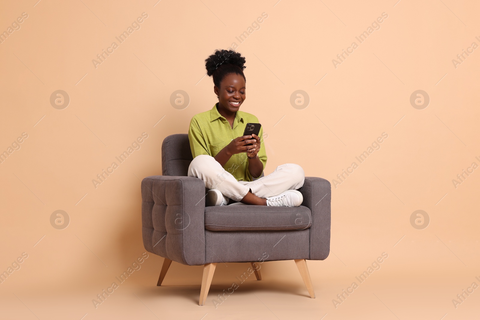 Photo of Smiling woman with smartphone sitting in armchair on beige background