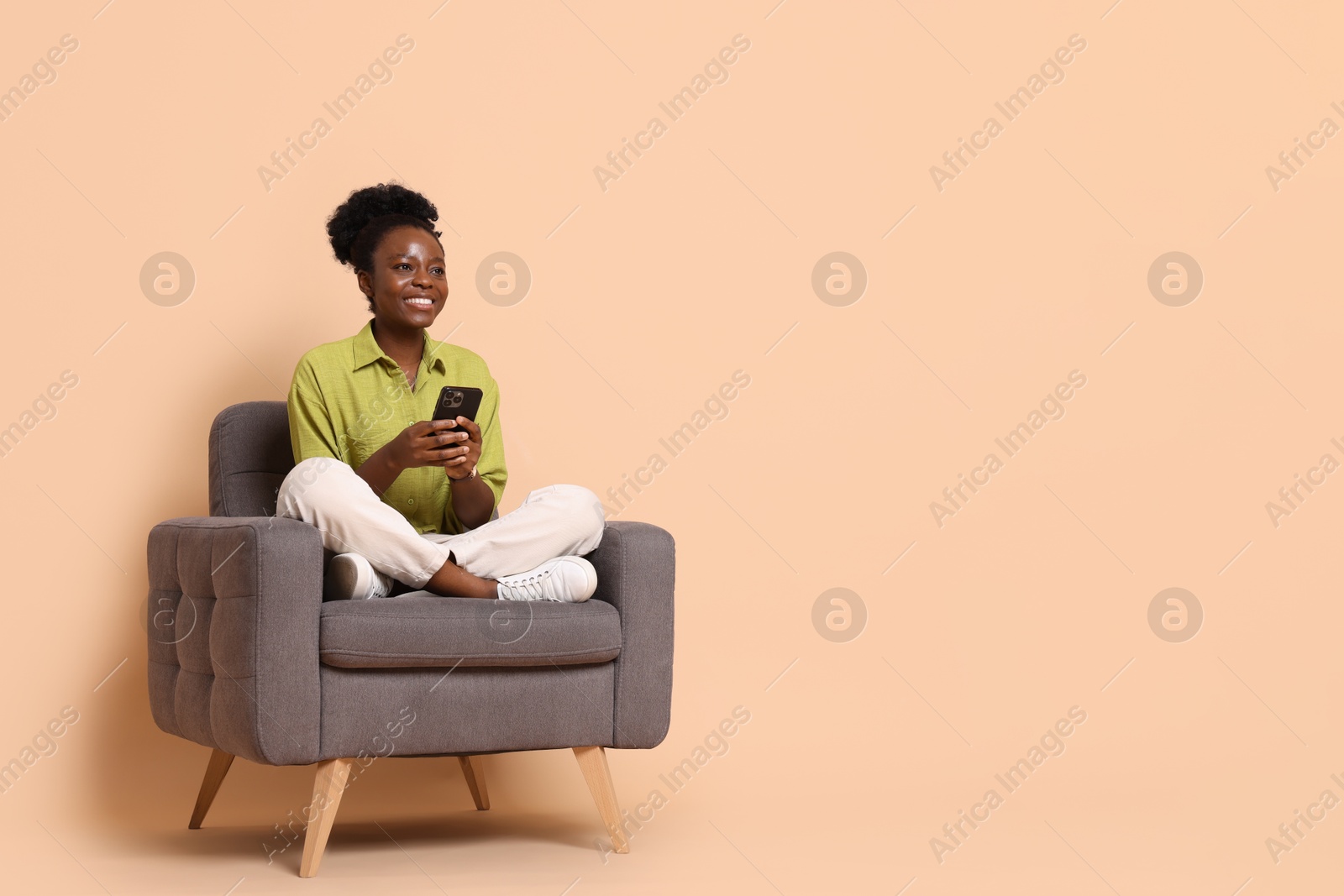 Photo of Smiling woman with smartphone sitting in armchair on beige background. Space for text