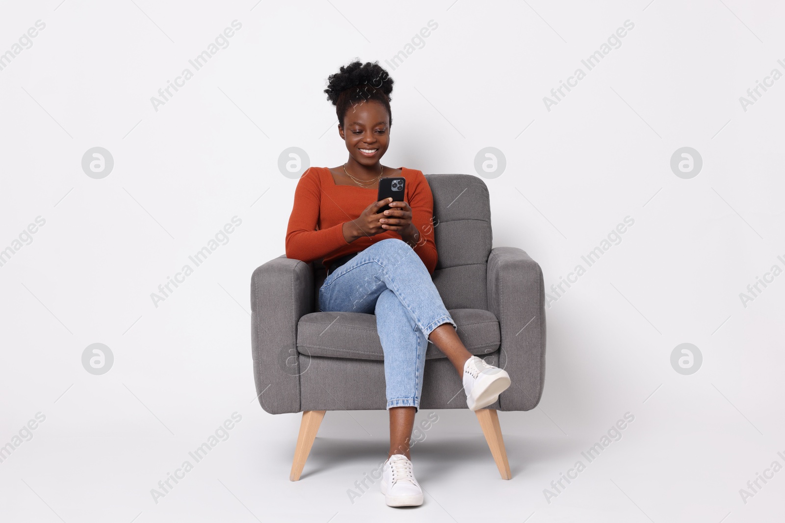 Photo of Smiling woman with smartphone sitting in armchair on white background