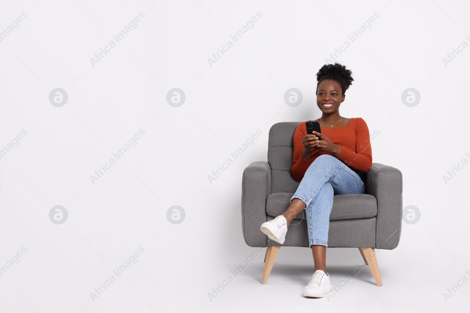 Photo of Smiling woman with smartphone sitting in armchair on white background. Space for text