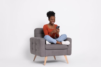 Photo of Smiling woman with smartphone sitting in armchair on white background