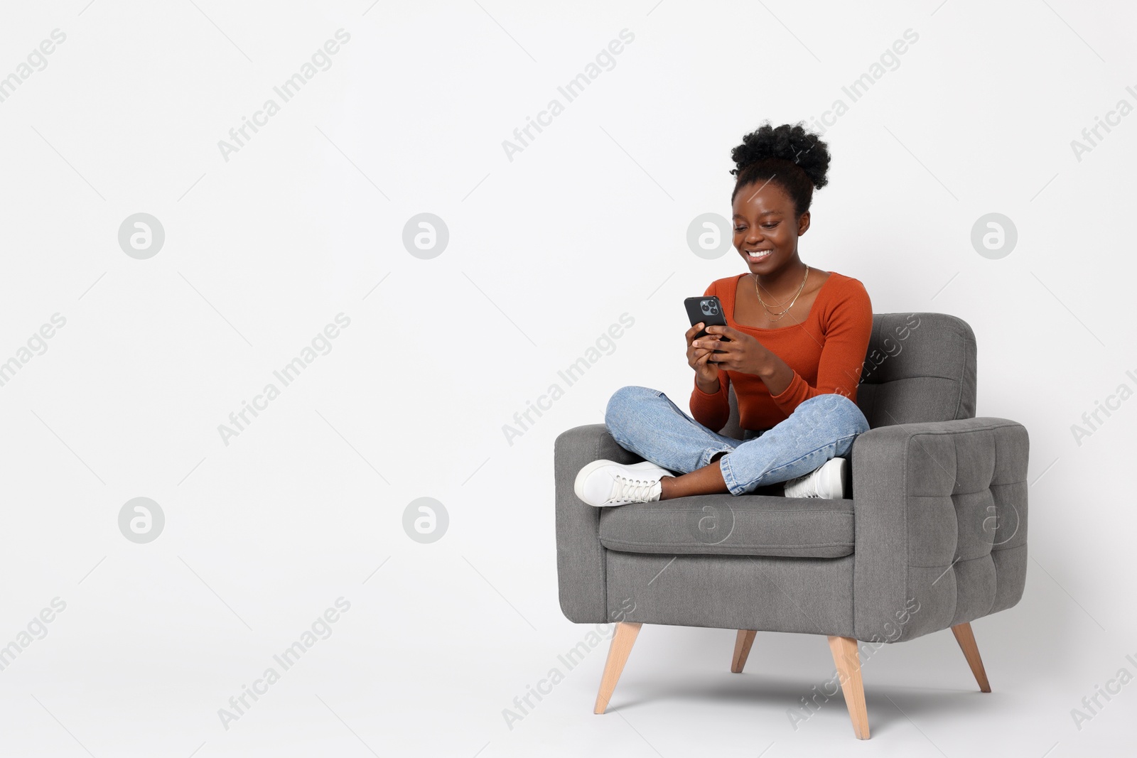 Photo of Smiling woman with smartphone sitting in armchair on white background. Space for text