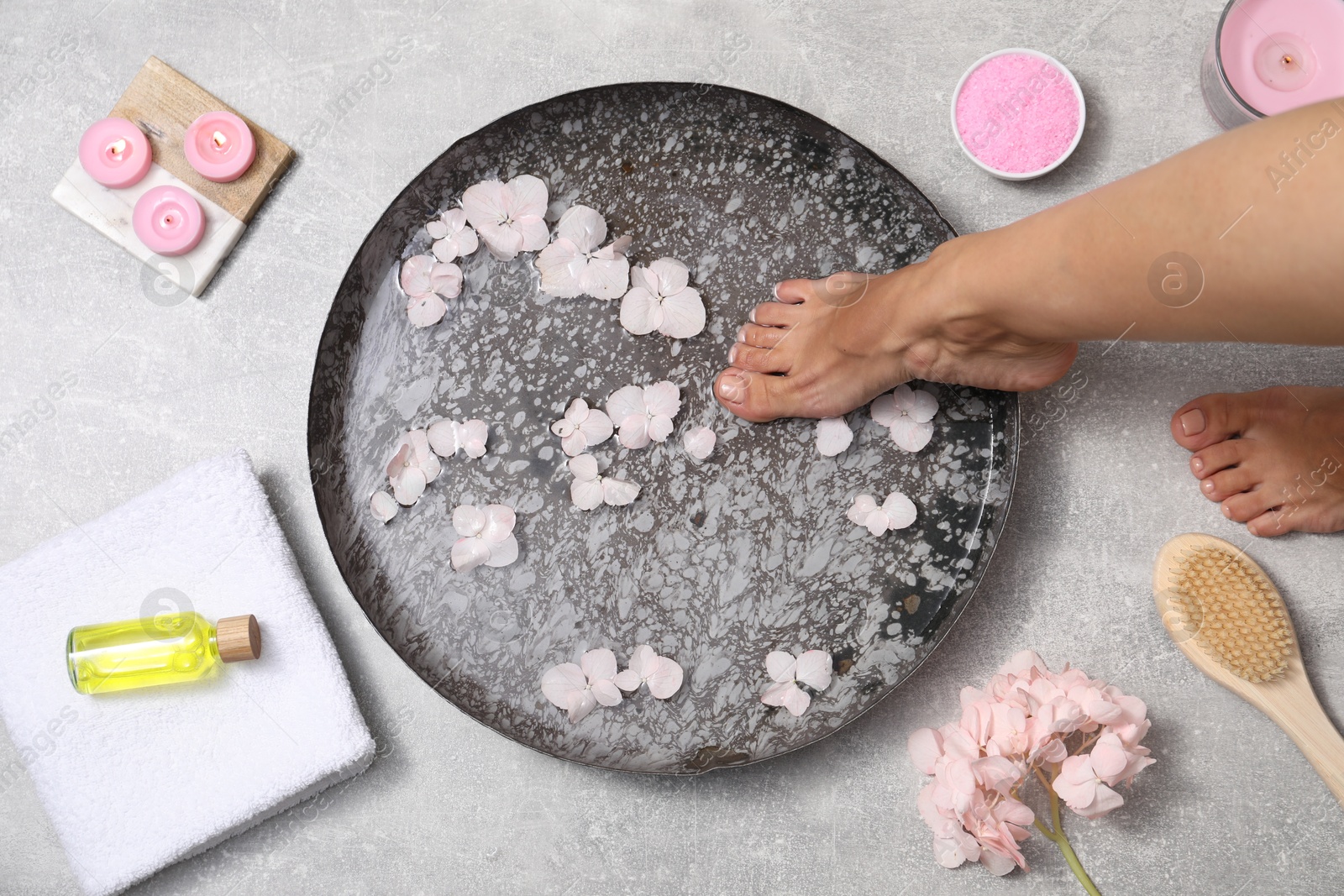 Photo of Woman soaking her feet in bowl with water and flowers on floor, top view. Spa treatment