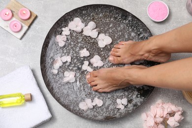 Photo of Woman soaking her feet in bowl with water and flowers on floor, top view. Spa treatment