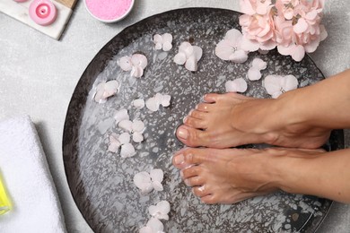 Photo of Woman soaking her feet in bowl with water and flowers on floor, top view. Spa treatment