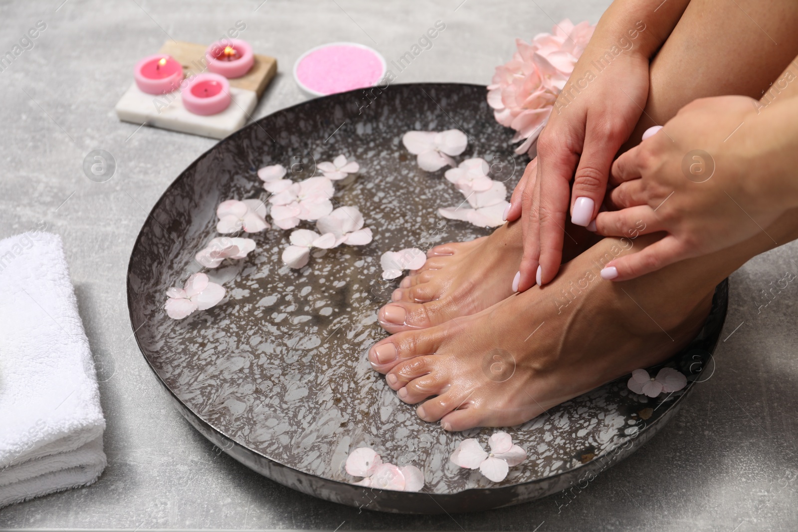 Photo of Woman soaking her feet in bowl with water and flowers on floor, closeup. Spa treatment