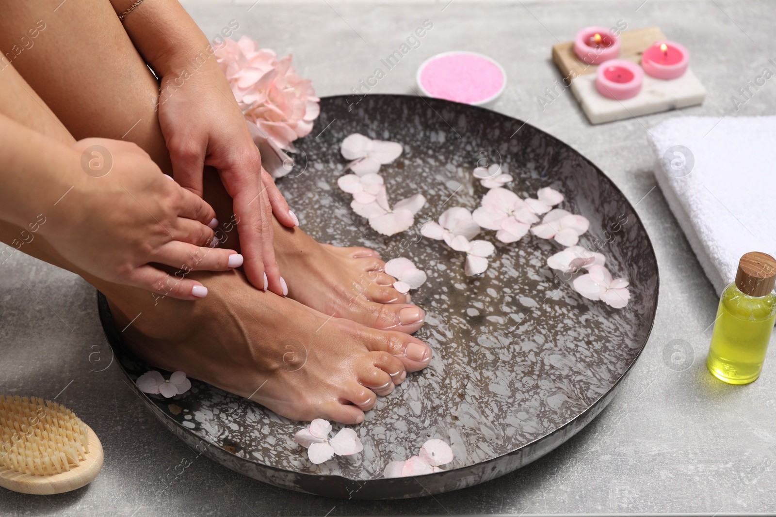 Photo of Woman soaking her feet in bowl with water and flowers on floor, closeup. Spa treatment