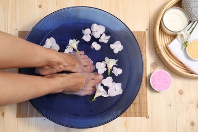 Photo of Woman soaking her feet in bowl with water and flowers on floor, top view. Spa treatment