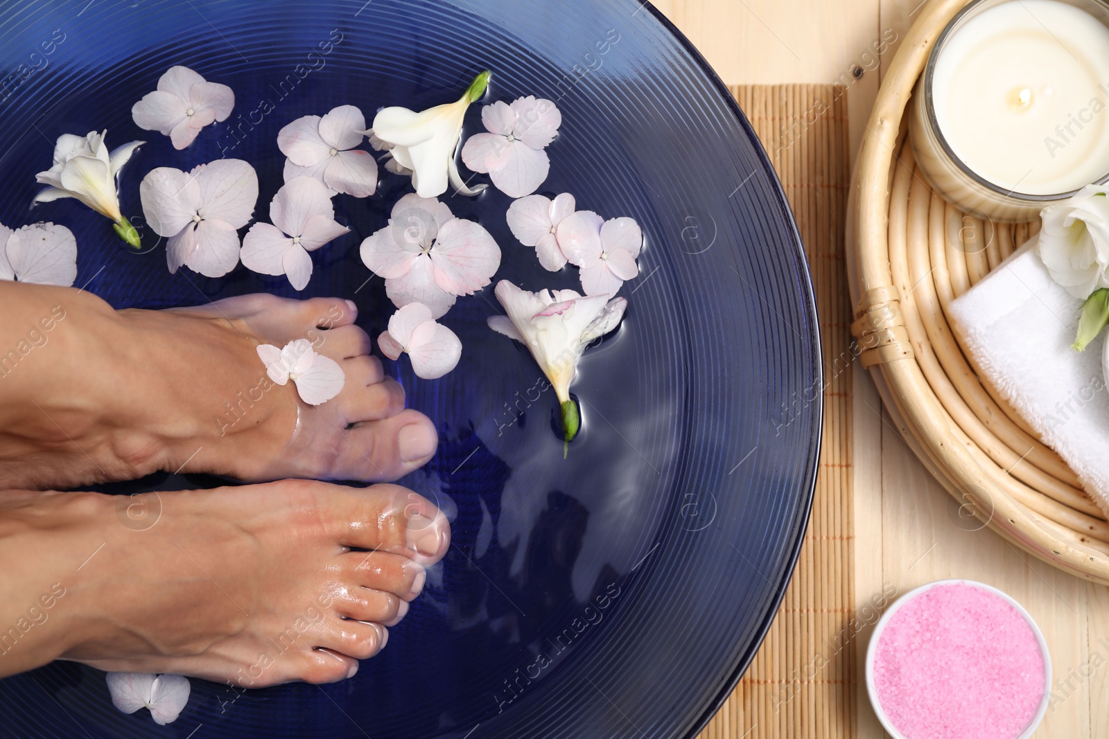 Photo of Woman soaking her feet in bowl with water and flowers on floor, top view. Spa treatment