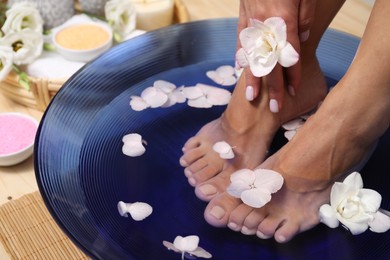 Photo of Woman soaking her feet in bowl with water and flowers on floor, closeup. Spa treatment