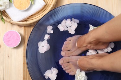 Photo of Woman soaking her feet in bowl with water and flowers on floor, top view. Spa treatment