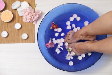 Photo of Woman soaking her feet in bowl with water and flowers on floor, top view. Spa treatment