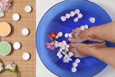 Photo of Woman soaking her feet in bowl with water and flowers on floor, top view. Spa treatment