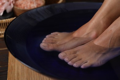 Photo of Woman soaking her feet in bowl with water on floor, closeup. Spa treatment