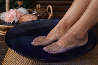 Photo of Woman soaking her feet in bowl with water on floor, closeup. Spa treatment