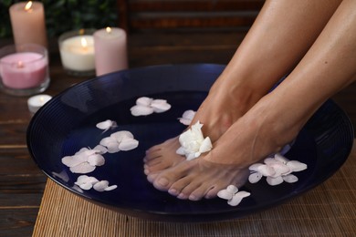 Photo of Woman soaking her feet in bowl with water and flowers on floor, closeup. Spa treatment