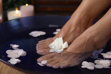 Photo of Woman soaking her feet in bowl with water and flowers on floor, closeup. Spa treatment