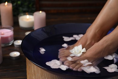 Photo of Woman soaking her feet in bowl with water and flowers on floor, closeup. Spa treatment