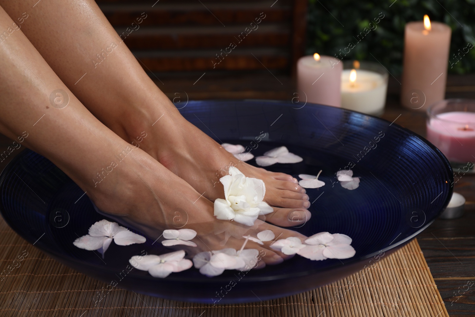 Photo of Woman soaking her feet in bowl with water and flowers on floor, closeup. Spa treatment