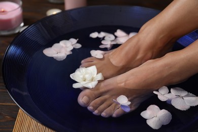 Photo of Woman soaking her feet in bowl with water and flowers on floor, closeup. Spa treatment