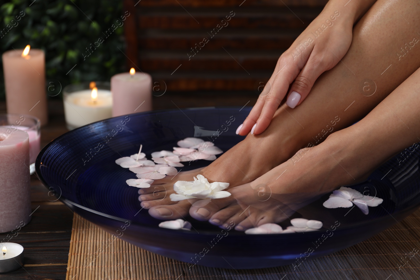 Photo of Woman soaking her feet in bowl with water and flowers on floor, closeup. Spa treatment