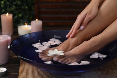 Photo of Woman soaking her feet in bowl with water and flowers on floor, closeup. Spa treatment