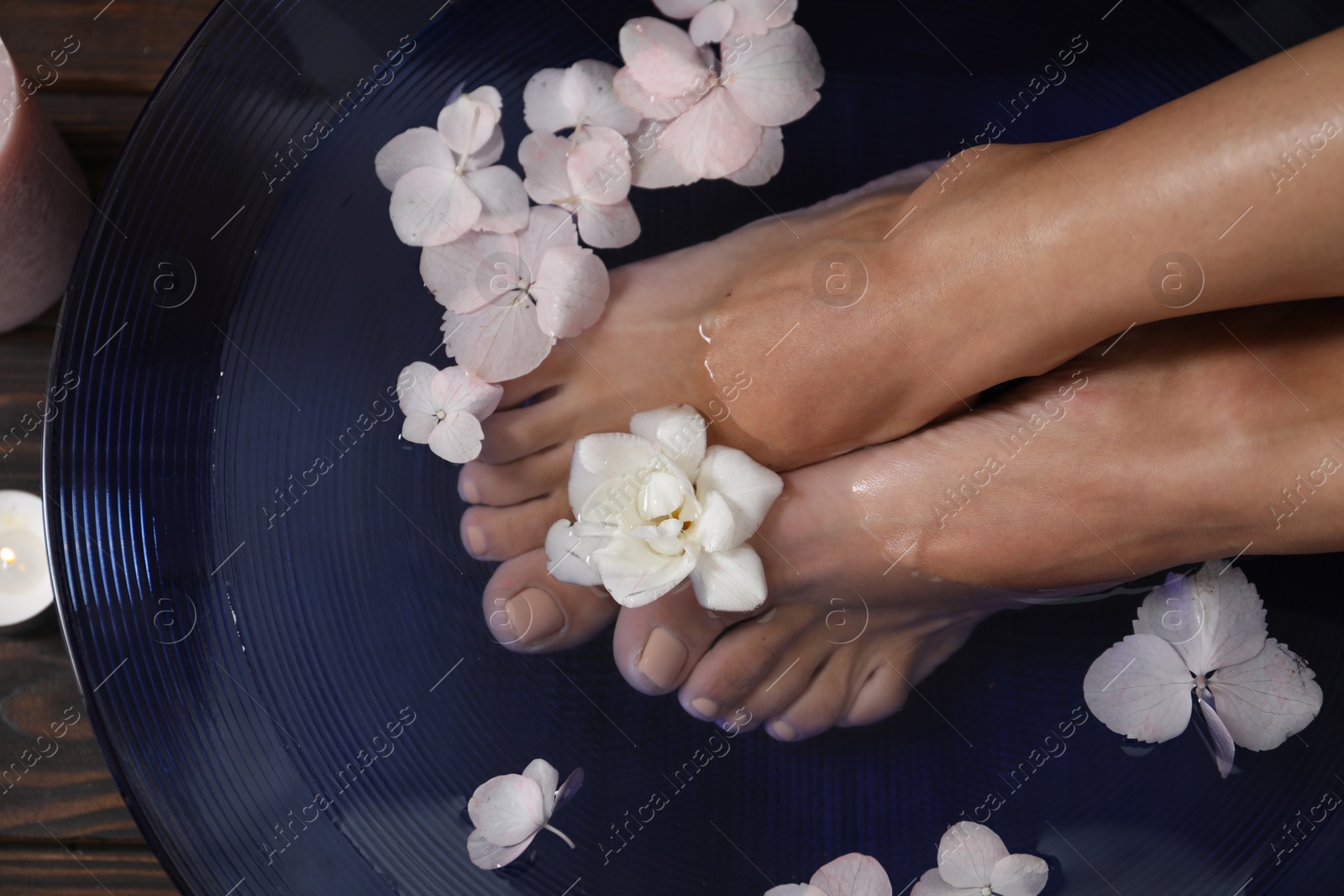 Photo of Woman soaking her feet in bowl with water and flowers on floor, top view. Spa treatment