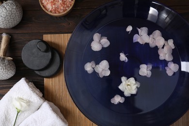 Photo of Bowl of water with flowers and different spa supplies on wooden table, flat lay