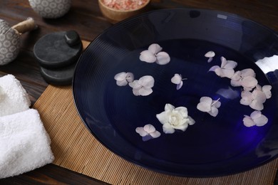 Photo of Bowl of water with flowers and different spa supplies on wooden table, closeup