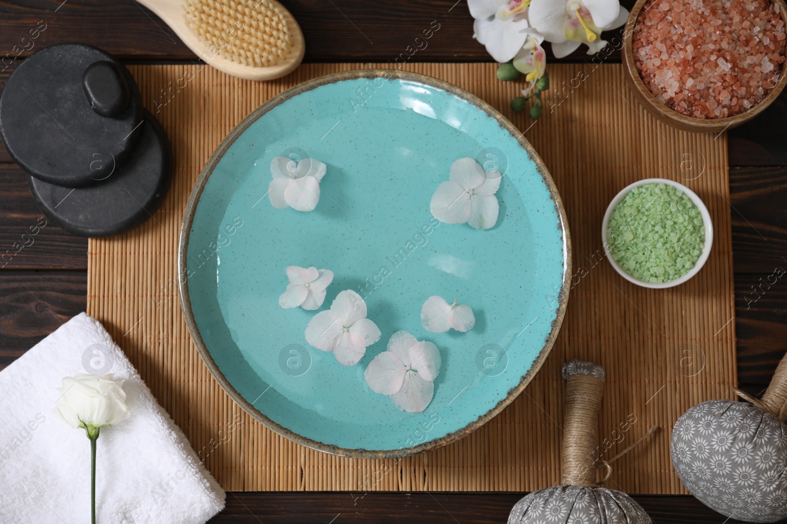 Photo of Bowl of water with flowers and different spa supplies on wooden table, flat lay