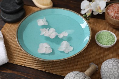 Photo of Bowl of water with flowers and different spa supplies on wooden table, closeup